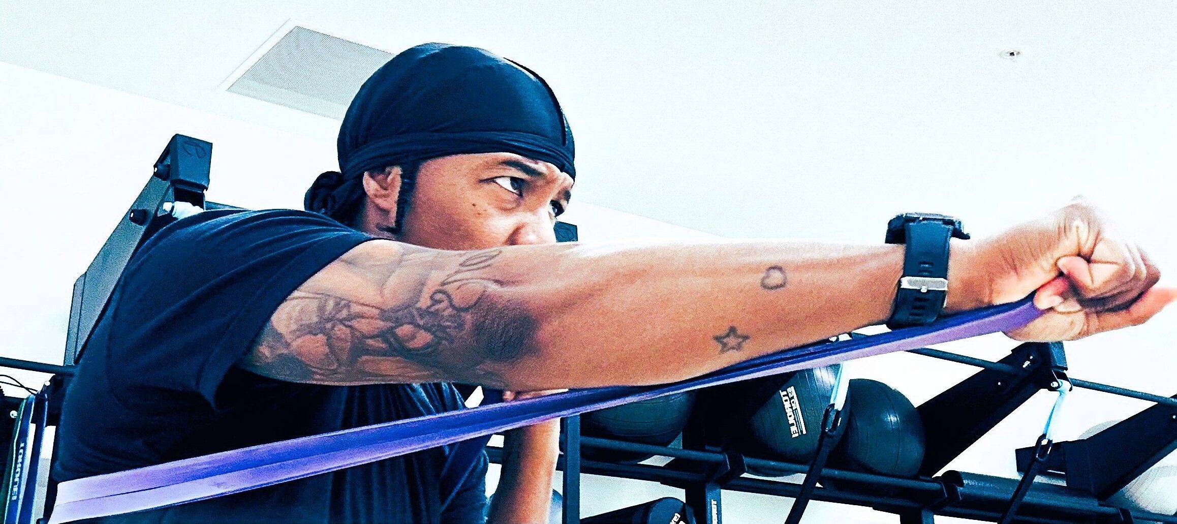 Rahsh aka Cold Work the Pro Boxer wearing a black head wrap training with a resistance band, extending their arm in a punching motion inside a gym.